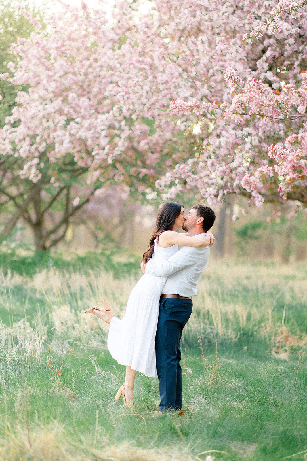 Husband and wife kissing in front of pink blooms as a spring photo session in Lincoln