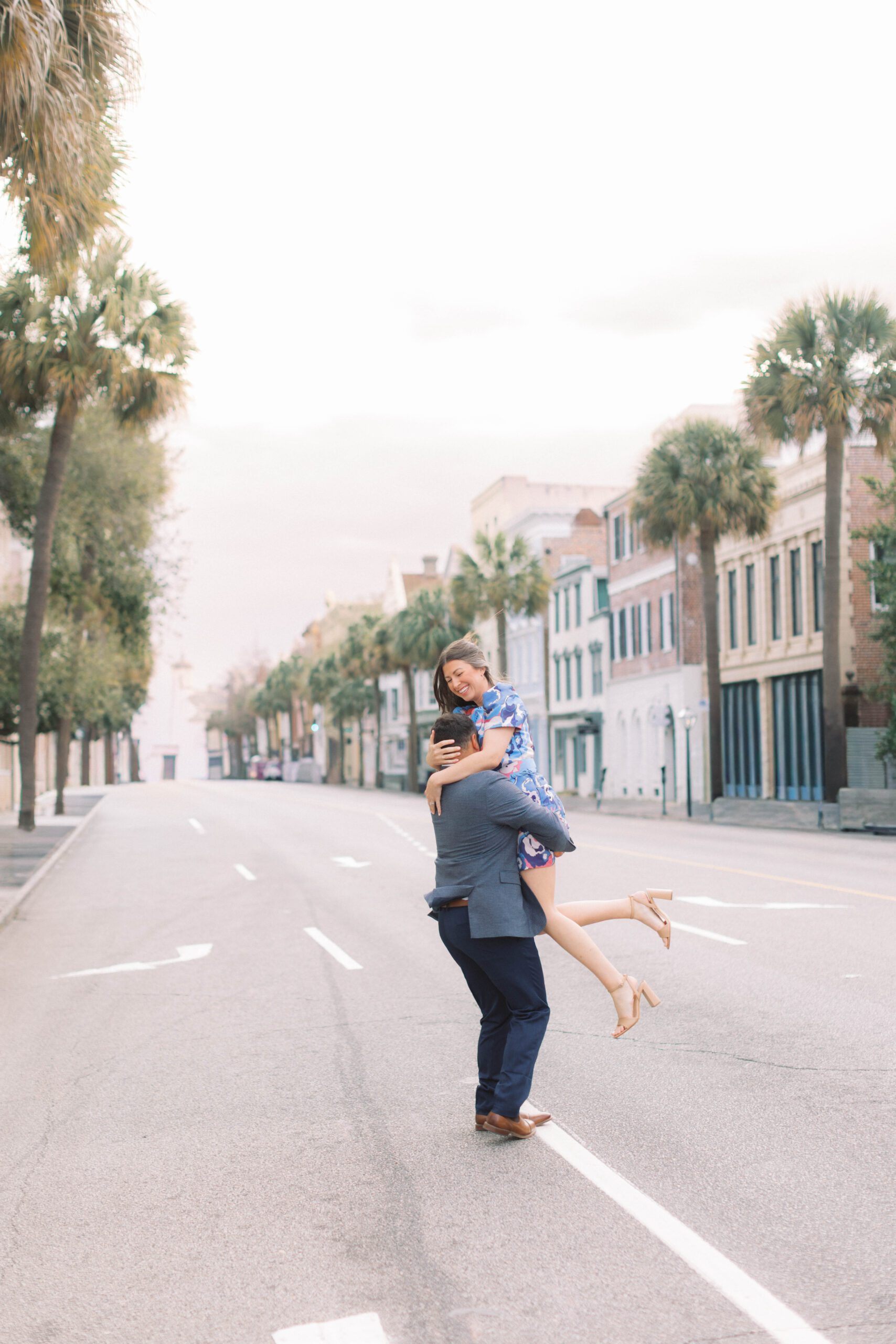Couple portrait session in Charleston at sunrise with husband lifting wife in the middle of a palm-lined historic street