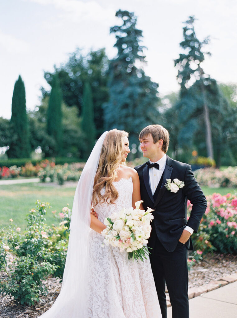 Bride with cathedral veil and bouquet beside her groom in an Omaha rose garden