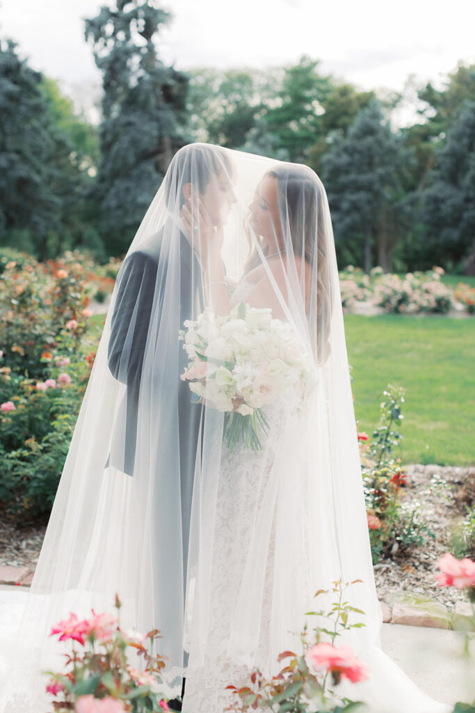 Bride and groom sharing a kiss under her cathedral veil in an Omaha rose garden