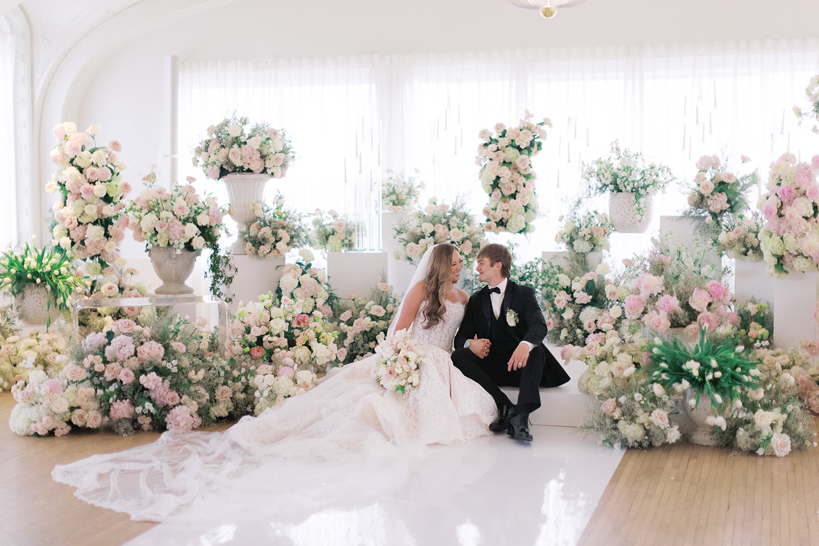 Bride and groom seated among blush and white garden florals in the Schimmel Ballroom at The Kimpton Cottonwood Hotel, Omaha