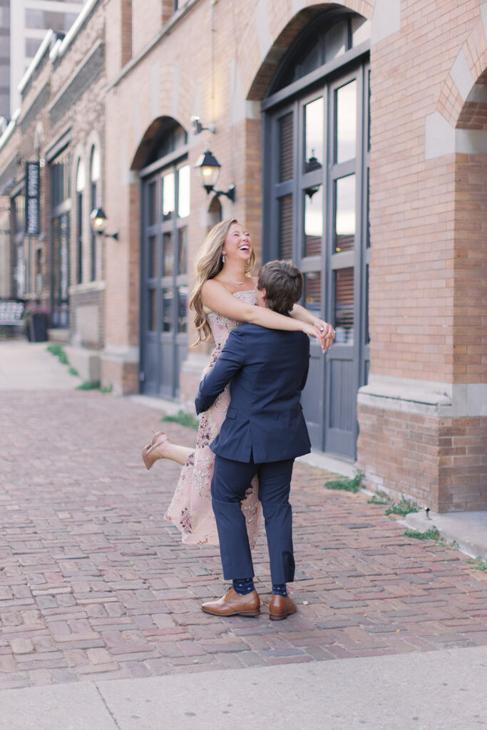 Groom lifting bride on a brick street in downtown Omaha during their Kimpton Cottonwood wedding weekend